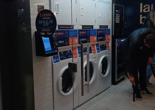 Lavanderia self-service com lavadoras e secadoras empilhadas e totem de pagamento