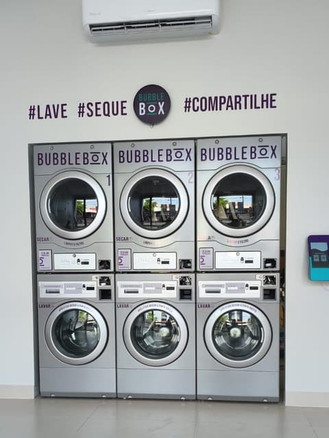 Parede com três secadoras empilhadas sobre três lavadoras numa lavanderia self-service recém-instalada