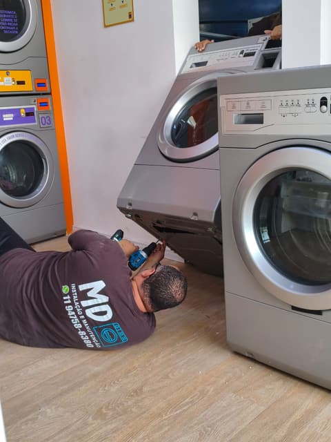Daniel, de camiseta da M&D, montando a base de uma lavadora profissional deitado no chão