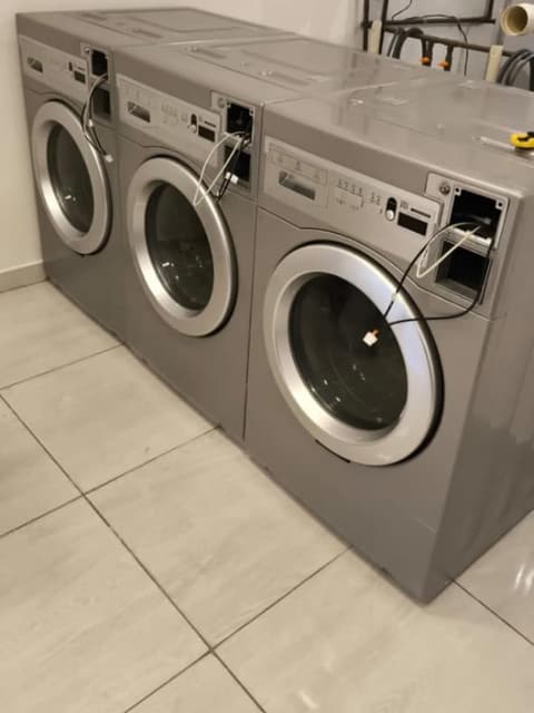 Três lavadoras profissionais com os cabos do sistema de pagamento saindo do painel